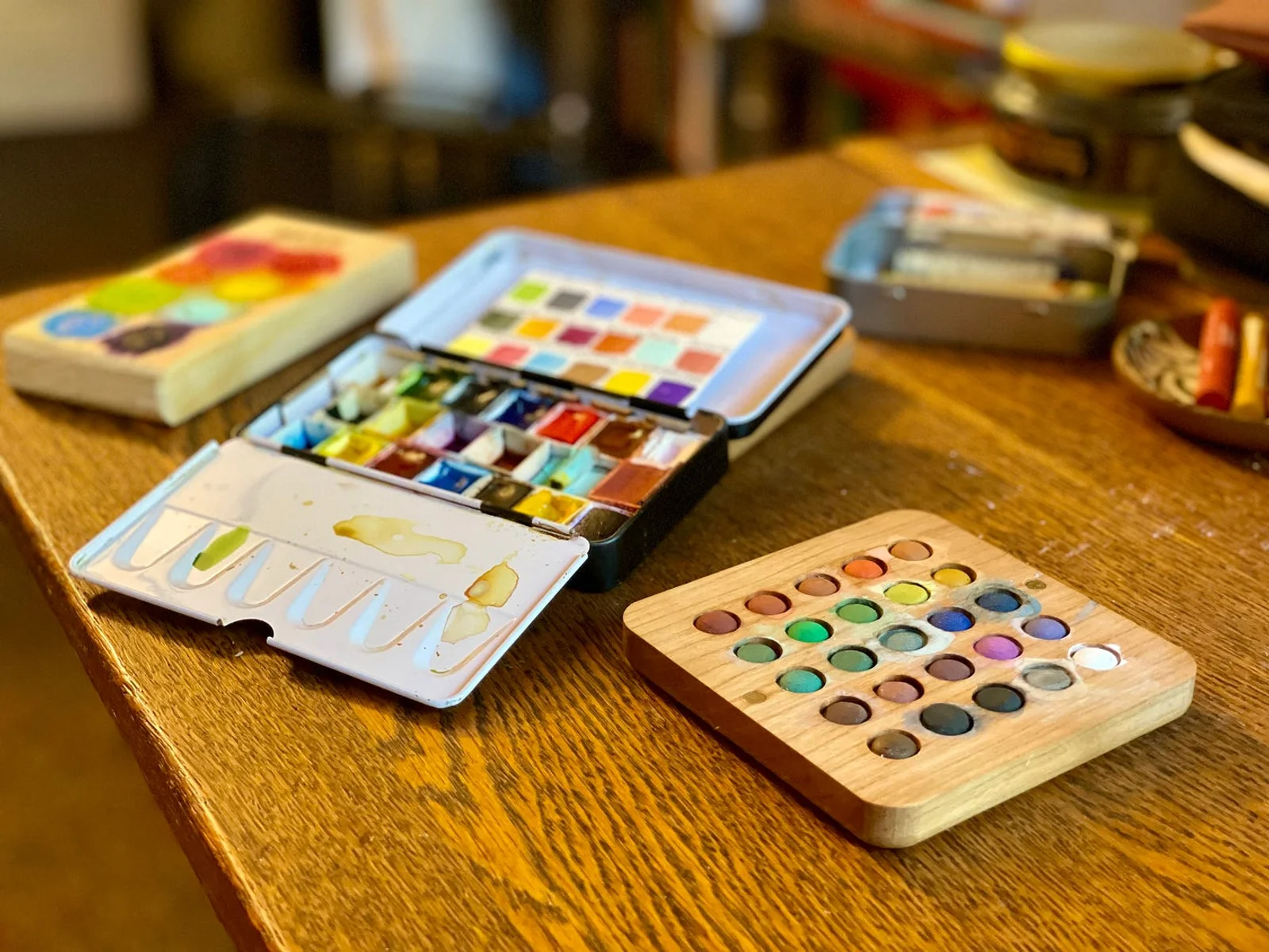 Three watercolor palettes laying on a desk.