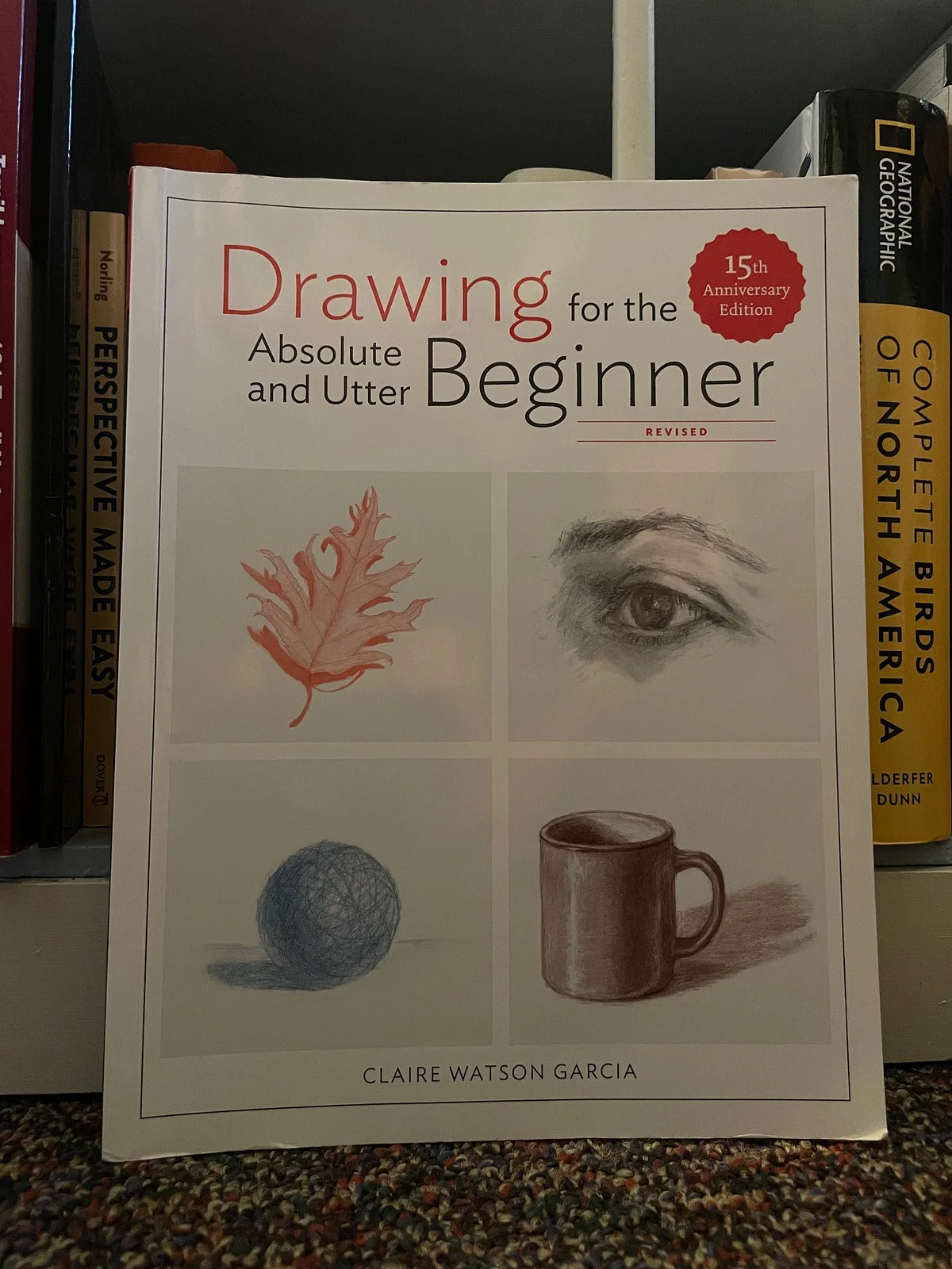 Book set against shelf. Titled Drawing for the Absolute and Utter Beginner, by Claire Watson Garcia.