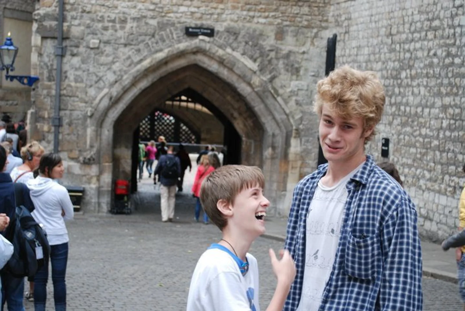Two boys stand outside the Tower of London. The short one on the left looks up at his brother, laughing. The tall one on the right makes a funny face at the camera.